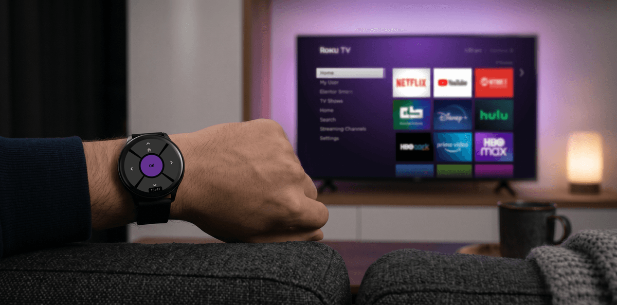Hand wearing a smartwatch showing a purple Roku D-pad remote in front of a Roku TV